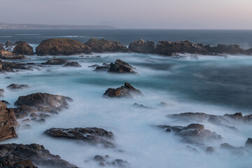 long exposure of a rocky shore with breaking waves on sunset light