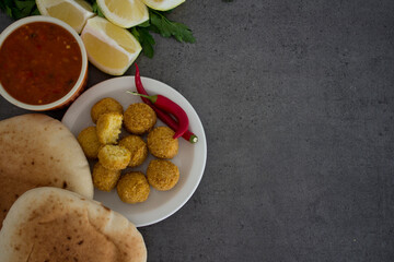 Falafel - authentic food of Israel. Fresh ingredients top view: plate of falafels, pita bread, parsley, harissa sauce, lemon, parsley and red pepper.  Dark grey background with copy space. 