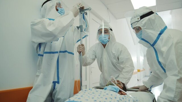 Paramedics doctors in face masks body suits mobing stretcher bed with sick patient suffering coronavirus symptoms running in hospital corridor. Pandemic. Emergency department.