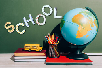 Globe and pen holder on notebook near toy school bus on books near green chalkboard with school lettering