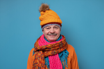 Handsome caucasian funny man in several hats and scarfs on blue background