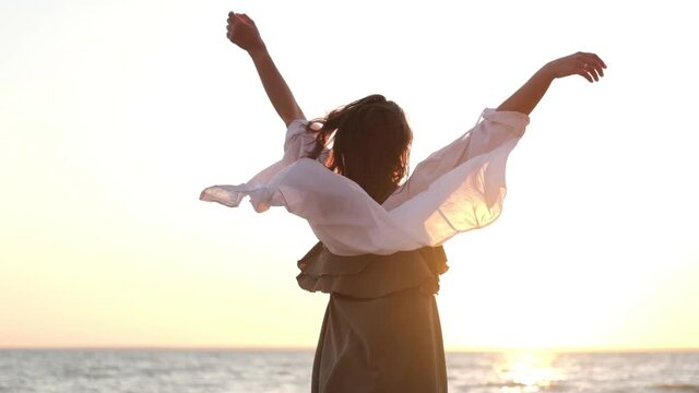 beautiful girl dancing on the beach in a white shirt. Free girl with long hair in a white shirt dances in the sunset. Healthy woman dancing on the beach.