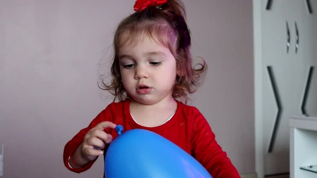 Crian&ccedil;a com roupa vermelha brincando feliz com um bal&atilde;o azul. Video gravado em camera lenta. 