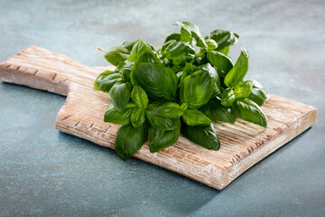 Bunch of fresh organic basil in cutting board on rustic wooden background