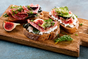 Variety of mini sandwiches with cream cheese, vegetables and salami.