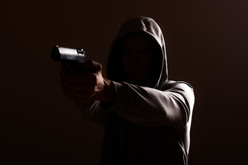 dangerous hooded man threatens with a pistol shot in his hands