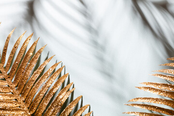 Gold palm leaves and shadows on a blue wall background.
