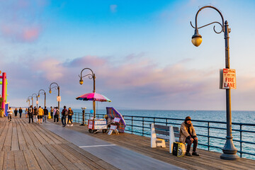 Beautiful evening sky sunset in Santa Monica, California. People/ tourists walk and shop at leisure, small business vendors offer service/ items for sale.