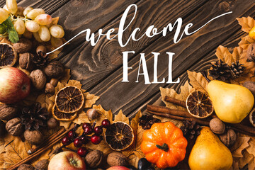 Top view of autumnal harvest and foliage near welcome fall lettering on brown wooden background