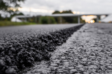 A large layer of fresh hot asphalt. Layer of asphalt raw material in a shallow depth of field. Rollers rollin fresh hot asphalt on the new road. Road construction. Construction of a new road.