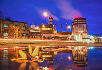 Naklejka premium A panoramic view of the pipes and cooling towers of the CHP. Industry district at night, reflection in water.