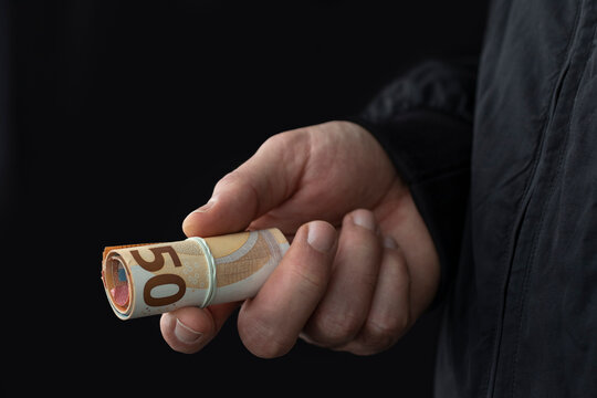 Close up of male hand offering cash on black background. Illegal smuggling concept.