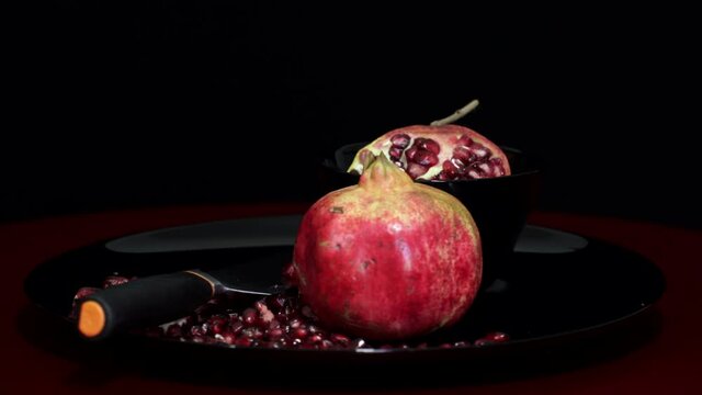 Pomegranate fruit and seeds on black plate with knife rotating on black background