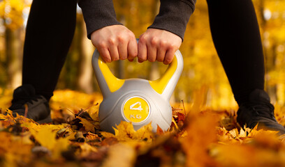Young girl holding heavy kettlebell in a beautiful, vibrant colors autumn park. Healthy fitness...