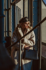 Outdoor fashion portrait of elegant woman wearing faux fur teddy bear coat, leather beret, holding...