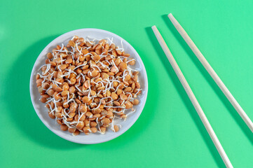 plate with lentil sprouts and chopsticks on a green table