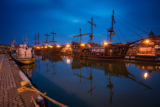 Poland, Pomerania, Leba, Historic tall ships moored at harbour at dusk