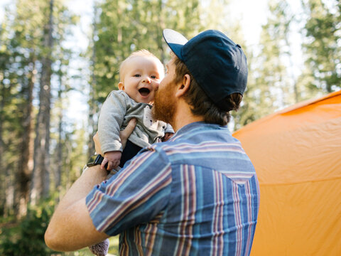 Man kissing baby son (6-11 months) in forest, tent in background, Wasatch Cache National Forest