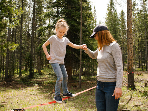 Mother assisting daughter (6-7) walking on slackline in forest, Wasatch-Cache National Forest