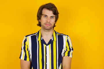 Joyful Young handsome Caucasian man, wearing stripped shirt standing against yellow wall looking to...