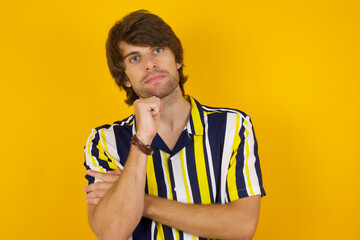 Portrait of thoughtful Young handsome Caucasian man, wearing stripped shirt keeps hand under chin, looks away trying to remember something or listens something with interest. Youth concept.