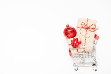 Shopping cart with gifts and christmas ball on white background with copy space.