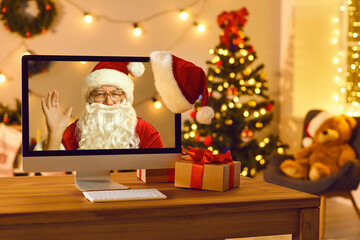Computer standing on table in cozy room with old Father Christmas on screen waving hand