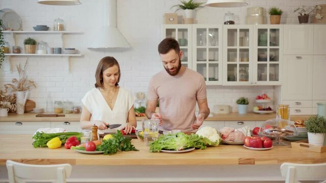 Young couple cooking together preparing dinner chopping vegetables and talking at home 