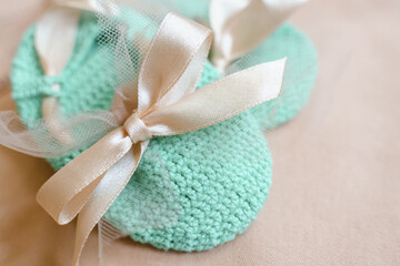 Crochet baby booties in mint color with a beige satin bow. Close-up, selective focus. Baby girl waiting concept.