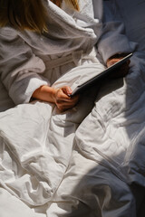 Fototapeta premium Woman holds tablet in hands. Relaxed in bed. Morning online activities in home. Watching movies and TV shows on mobile device. Social media addiction. Work at home, freelance. Technology in lifestyle