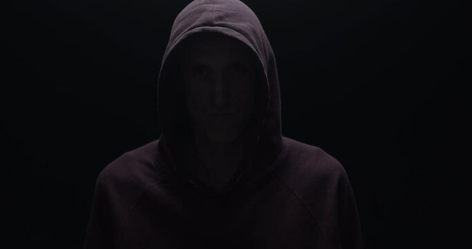 Silhouette of a man with a darkened face in a hood on a black background. A portrait of a murderer, a hacker.