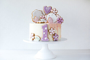 White birthday cake decorated with gingerbread in the form of a heart, bird and flowers for a little girl on a white background