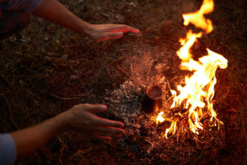 A man warms his hands by a forest fire.