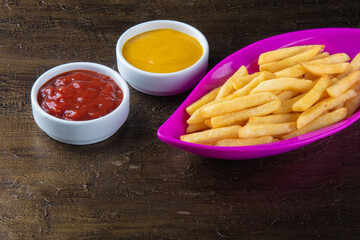 Delicious french potato fries in a pink bowl with ketchup and mustard sauces.