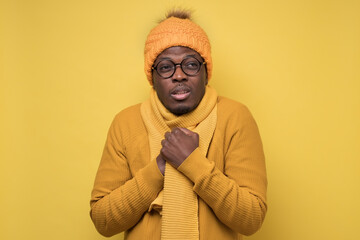 Funny african american mature man in yellow scarf and hat freezing in warm clothing. Studio shoot...