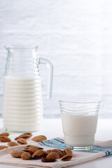 Almond milk in a glass with almonds on a white table