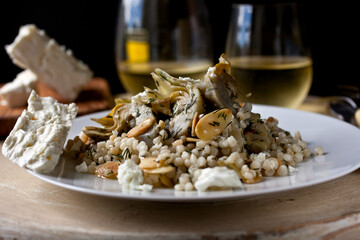 Close up of fregola with artichokes, feta, toasted almonds and herbs served on plate