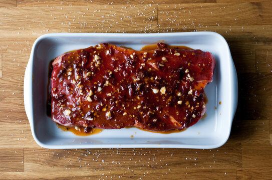 Overhead view of marinated raw meat steak with spices in baking tray