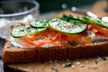 Close up of smoked salmon sandwich with goat cheese and cucumber served on cutting board