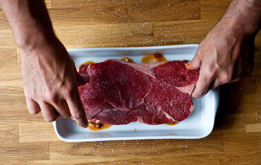 Overhead view of man's hands putting marinated raw meat steak in tray