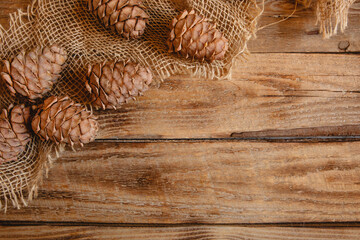 Scattered fir cones and burlap on a wooden background. Christmas flat layout with space for text