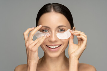 Happy woman applying hydrogel under-eye recovery patches enriched with collagen, vitamin E, provides intensive hydration and diminishes the signs of aging, helps reduse eye puffiness. Skincare beauty.