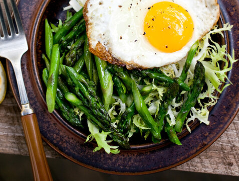 Close up of pan seared asparagus salad with frisee and fried egg served on plate