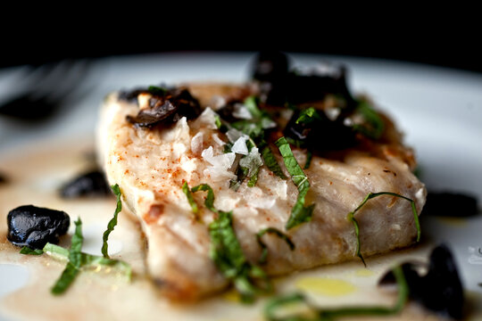 Close up of seared blackfish with tomato water, herbs and olives served on plate