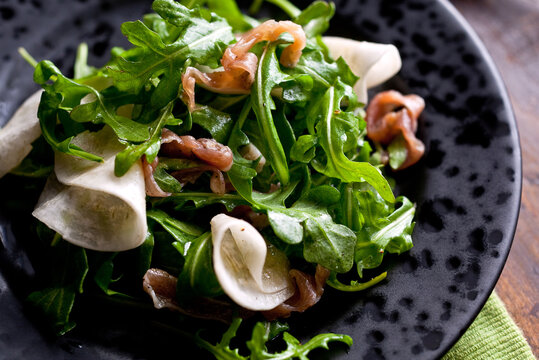 Close up of turnip salad with arugula and prosciutto served on plate