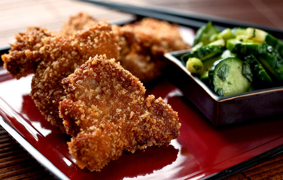 Close up of pork katsu with pickled cucumbers and shiso served on plate