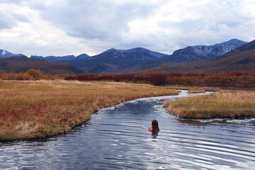 Kamchatka in autumn. A woman bathes in the hot springs of Nalychevo overlooking the volcanoes.