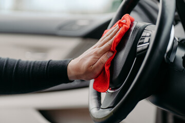 Mans hand cleaning luxury car interior. Wiping steering wheel during coronavirus. Washing auto from...