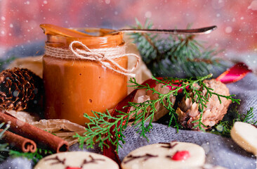 Fototapeta na wymiar A small jar with boiled homemade condensed milk. Shortbread Christmas cookies, lights, sprigs of spruce, bumps.