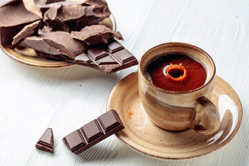 Hot chocolate and broken pieces of bitter chocolate on a white wooden table.